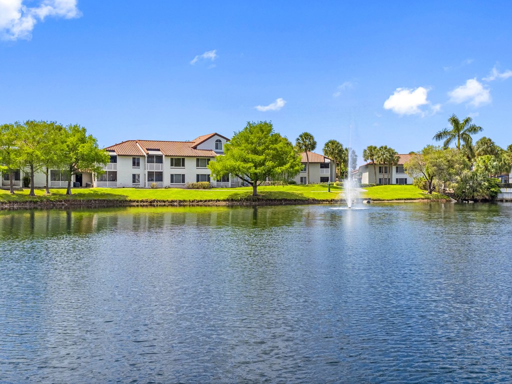 A serene lake with a fountain in the middle of it and a building in the background.
